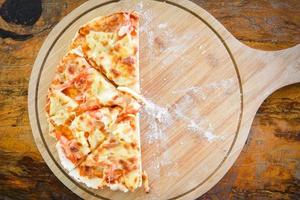 zelfgemaakte pizza-pizza italiaans wordt traditioneel gekookt - pizzakaasplak op houten dienblad en geserveerd op een houten tafel, bovenaanzicht foto