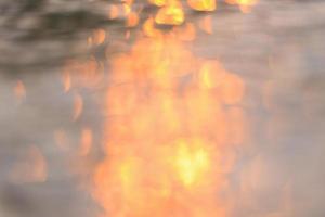 abstract zonlicht reflecterend op de achtergrond van het water, licht bokeh op het wateroppervlak bij zonsondergang natuur zomer of lente oceaan zee foto