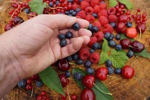 vrouwelijke hand met bessen. bosbes, framboos, kers en aalbes op de houten tafel in de tuin. foto