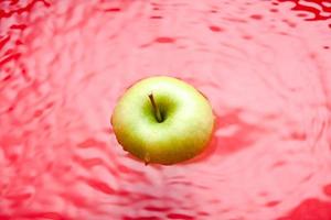 zwemmende appel op rode achtergrond. wateroppervlak met een zwemmende groene appel. foto