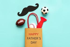 gelukkige vaderdag. bovenaanzicht van boodschappentas met valse snor, valse vlinderdas en sportballen. vaderdag viering concept foto