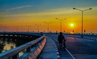 mensen ontspannen op gebogen kustweg met straatlantaarn en oranje lucht bij zonsondergang in chonburi, thailand. foto