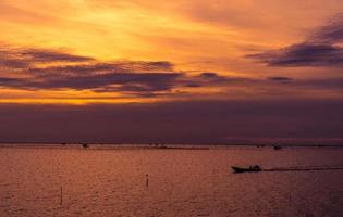 mooie dramatische zonsonderganghemel. donkere en oranje avondrood en wolken. natuur achtergrond voor rustig en vredig concept. tropische zee in de schemering. lange staart boot zeilen door visser. schoonheid in de natuur. foto