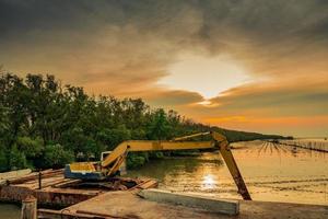 de graafmachine graaft langs de kust bij het mangrovebos om de pijp te plaatsen. mooie wolken en lucht op de bouwplaats foto