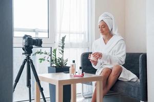 handdoek op het hoofd. voor de camera op het statief. conceptie van mode en huidverzorging. brunette meisje gebruikt cosmetica foto