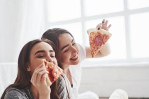 geluk zit in kleine dingen. zussen die pizza eten als ze tv kijken terwijl ze overdag op de vloer van een mooie slaapkamer zitten foto