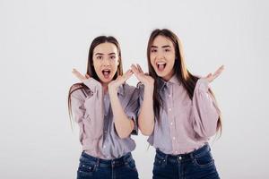 uitdrukking van verwondering. twee zussen tweeling staan en poseren in de studio met witte achtergrond foto