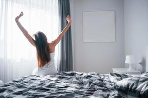 geweldige stemming. mooie jonge vrouw die 's ochtends in haar kamer op het bed zit foto