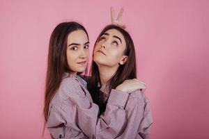 aan het dollen. twee zussen tweeling staan en poseren in de studio met roze achtergrond foto