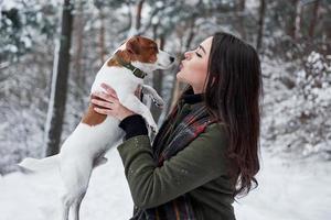 een lieve kus geven. lachende brunette die plezier heeft tijdens het wandelen met haar hond in het winterpark foto