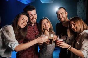 smaakt drankjes. groep jonge vrienden die glimlachen en een toast uitbrengen in de nachtclub foto