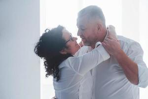 senior man en zijn vrouw in wit overhemd hebben een romantisch diner in de keuken foto