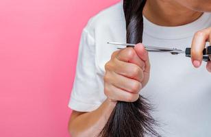 vrouwen die beschadigd en droog haar knippen. aziatische vrouw haar knippen met een schaar voor het doneren aan kankerpatiënten. haardonatie voor borstkanker persoon. vrouw met zwart lang haar op roze achtergrond. foto