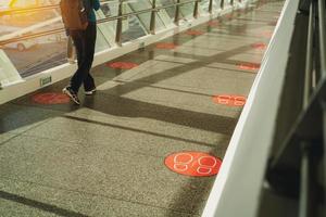 achteraanzicht van een vrouw die op een glazen voetgangersbrug loopt. gangverbindingen tussen gebouwen met symbolen voor sociale afstand op de vloer voor voetstap op afstand. voetstappen sticker stempel op brug vloer. foto