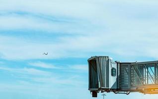 straalbrug na commerciële luchtvaartmaatschappij opstijgen op de luchthaven en het vliegtuig vliegen in de blauwe lucht en witte wolken. passagiersbrug voor vliegtuigen aangemeerd. vertrekvlucht van internationale luchtvaartmaatschappij. foto