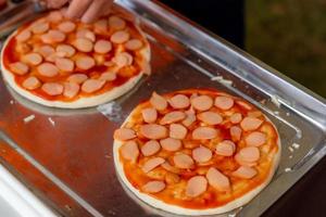 man maakt pizza in de keuken met pizzabodem en gesneden worst. twee stukken pizza op roestvrijstalen dienblad. fastfood en junkfood concept. ongezonde voeding. foto