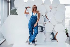 een zilverkleurig instrument. meisje in blauw uniform staat tegen abstracte muur met witte stukjes oppervlak in de vorm van zeshoek in de auto saloon foto