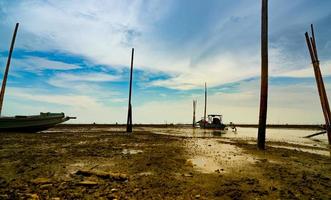 landschap van zee bij tij en blauwe lucht en wolken met vissersboot. zee modder strand wanneer het water lager. vissersboot geparkeerd aan de kust. levensstijl en cultuur van lokale vissers in thailand. foto