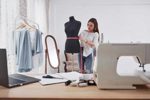 roze meetlint rond de taille van de mannequin. vrouwelijke modeontwerper werkt aan de nieuwe kleren in de werkplaats foto