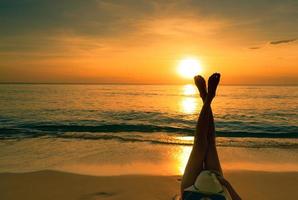 jonge Aziatische vrouw met hoed ontspannen op het strand bij zonsondergang. meisje liggend op zandstrand. op zijn kop vrouw blote voeten aan zee. alleen op vakantie. zomerse sferen. zomervakantie. tropisch paradijs strand. foto
