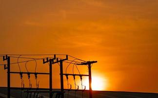 driefasige elektrische stroom voor overdracht van stroom door elektrische netten. hoogspanning elektrische palen in fabriek en dak van gebouw en oranje avondrood. elektrische stroom voor de ondersteunende verwerkende industrie. foto