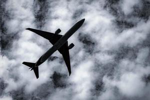 commerciële luchtvaartmaatschappij die op donkere lucht en witte pluizige wolken vliegt. onder het oog van vliegtuig vliegen. luchtvaartbedrijfscrisis door coronavirus. mislukte reis vakantie vlucht. luchttransport. trieste reis. foto