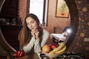 glimlachen en je goed voelen. mooie jonge vrouw die zich in de moderne keuken dichtbij gasfornuis bevindt foto