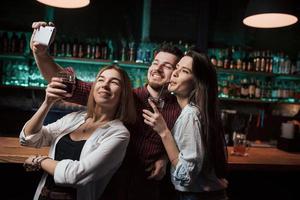 in de buurt van de bar met alcohol. vrienden nemen selfie in prachtige nachtclub. met drankjes in de handen foto