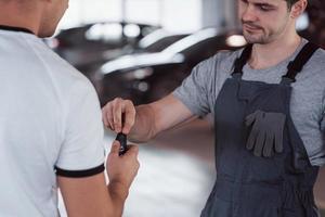 monteur geeft sleutels aan de eigenaar van de gerepareerde auto in de werkplaats foto