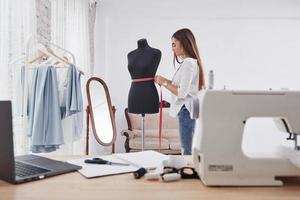 met roze meetlint op de taille van de mannequin. vrouwelijke modeontwerper werkt aan de nieuwe kleren in de werkplaats foto