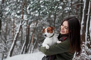 knuffel het huisdier en geniet van het moment. lachende brunette die plezier heeft tijdens het wandelen met haar hond in het winterpark foto