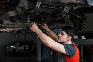 een stevige hand nodig. man in de werkplaats in uniform repareert kapotte delen van de moderne auto foto