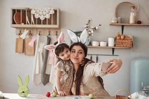 selfie maken. moeder en dochter in konijnenoren met Pasen hebben overdag plezier in de keuken foto
