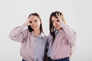 speelse stemming. twee zussen tweeling staan en poseren in de studio met witte achtergrond foto
