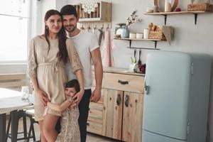 gelukkige jonge mensen. leuke familiefoto van zwangere moeder, vader en hun dochter. in de keuken staan foto