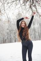 met handen omhoog. mooi meisje met lang haar en in zwarte blouse dansen in het winterbos foto