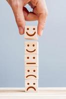 hand met glimlach gezicht symbool op houten kubus blokken. emotie, servicebeoordeling, ranking, klantbeoordeling, tevredenheids- en feedbackconcept foto