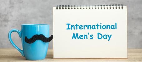 internationale mannendag met papieren notitieblok, blauwe koffiekop of theemok en zwart snordecor op tafel. gelukkig vaderdag en feestconcept foto