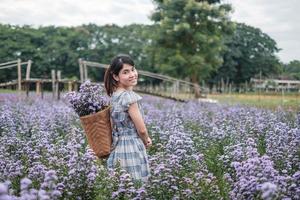 gelukkige vrouw toerist in blauwe jurk genieten in paarse margaret bloementuin. reizen, natuur, vakantie en vakantieconcept foto