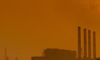 elektriciteitscentrale met oranje avondrood en vogels die in de lucht vliegen. luchtvervuiling concept. energie voor ondersteunende fabriek op industrieterrein. kracht en energie. stof verspreid in de lucht in de avond. foto
