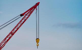 rupskraan tegen blauwe lucht en witte wolken. onroerend goed branche. rode rupskraan gebruikt haspelliftapparatuur op de bouwplaats. kraan te huur. kraandealer voor bouwbedrijven. foto