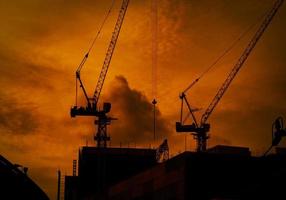 bouwkranen op hoogbouw met dramatische oranje lucht en wolken bij zonsondergang in de avond. bouwplaats van commercieel gebouw of condominium in de stad. architectuur achtergrond. foto