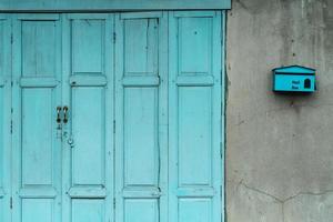 gesloten groene of blauwe houten deur en lege brievenbus op gebarsten betonnen muur van huis. oud huis met gebarsten cementmuur. vintage voordeur abstracte achtergrond. verlaten oud huis. foto