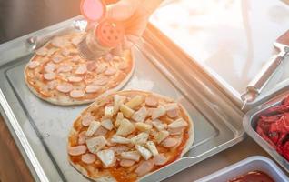 vrouw maakt pizza om te doneren bij liefdadigheidsevenement met pizzabodem en ananas. vrouwelijke chef-kok bereidt pizza met handen die de ingrediënten voor de pizza in dienblad op de houten tafel legt. voedsel voorbereiding foto