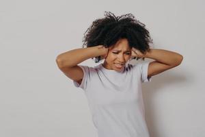 jonge boze geërgerde Afrikaanse vrouw die haar oren met beide handen bedekt om hard geluid te vermijden foto