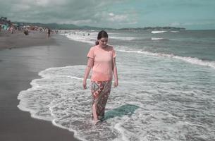 mooie jonge Spaanse vrouw die alleen op het strand loopt in een roze jurk tijdens een zonnige ochtend foto