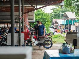 chiang mai, thailand, 2021 een aziatische man van middelbare leeftijd staat ernstig naar een oude motorfiets te kijken. foto