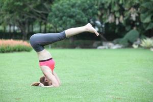 jonge vrouw in headstand yoga pose op gazon foto