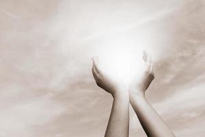 opgeheven handen die zon op bewolkte hemel vangen. concept van spiritualiteit, welzijn, positieve energie foto