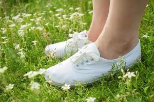 jonge vrouw in witte klassieke sneakers die in het gras op de lenteweide staan foto